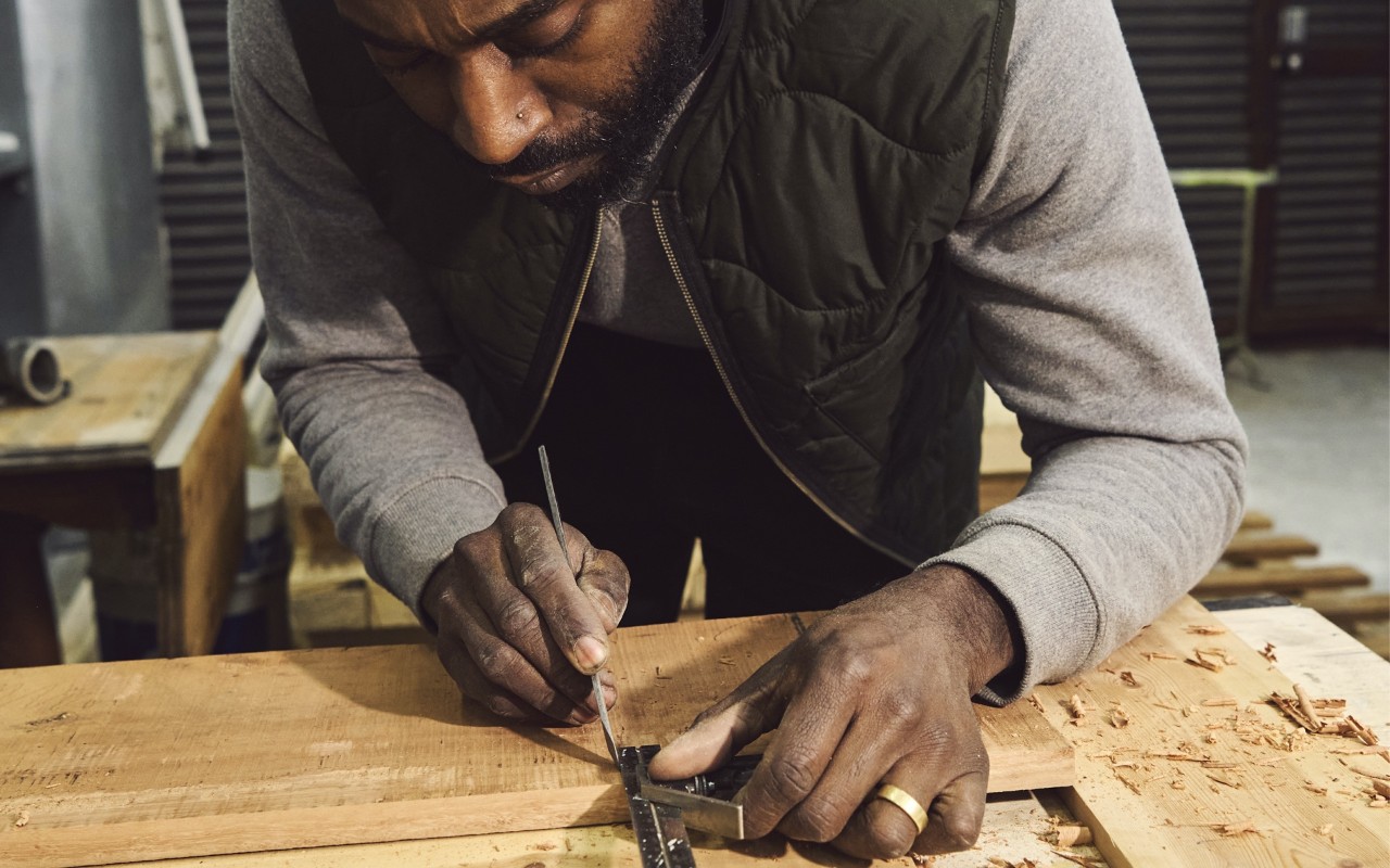 A man carefully measures something out at a woodworking bench.
