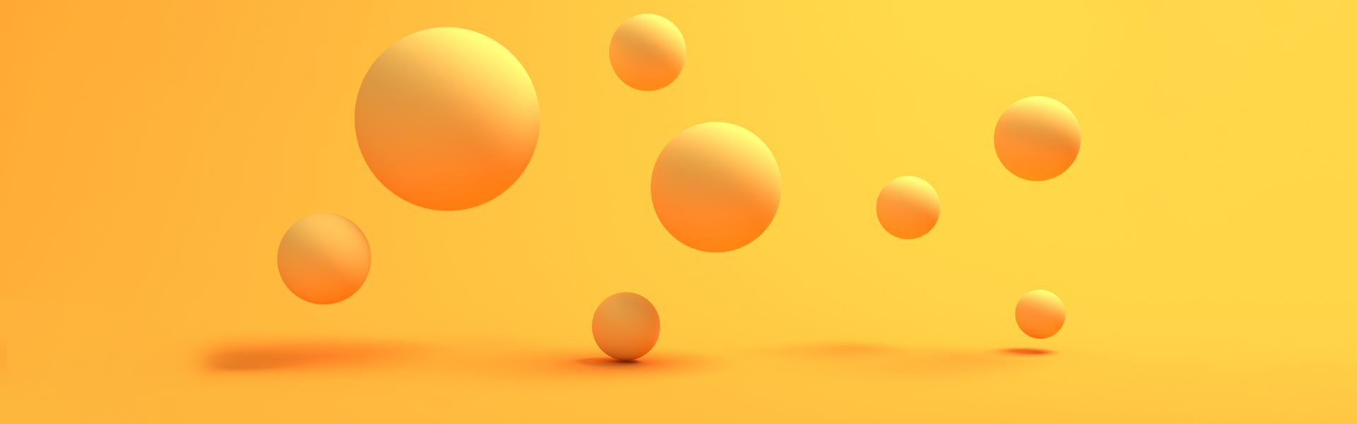 Photo showing a group of yellow spheres in different sizes suspended in mid-air against a yellow background.