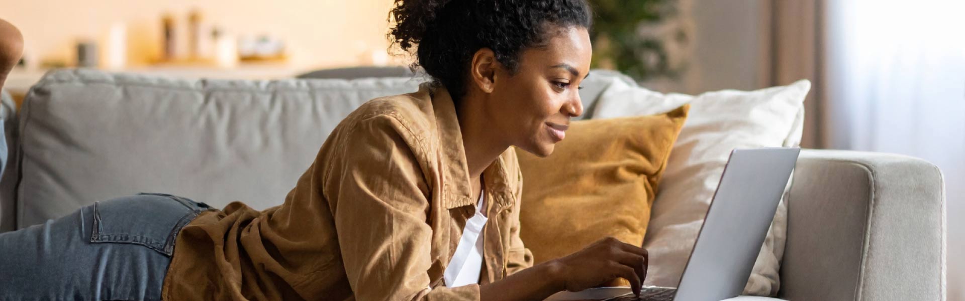 Smiling woman with laptop laying on couch.