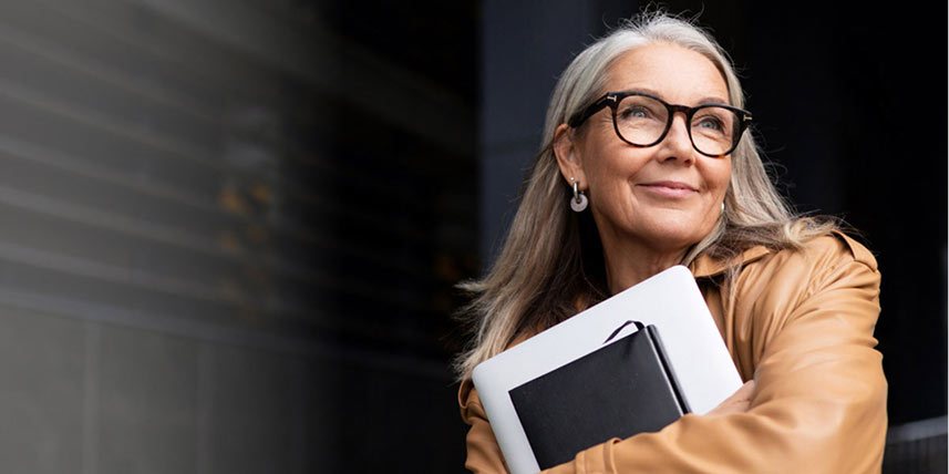 Woman holding a laptop and journal in her arms while smiling.