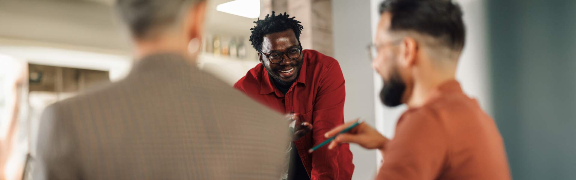 A man wearing glasses and dressed in a red shirt shares a laugh with his work colleagues.
