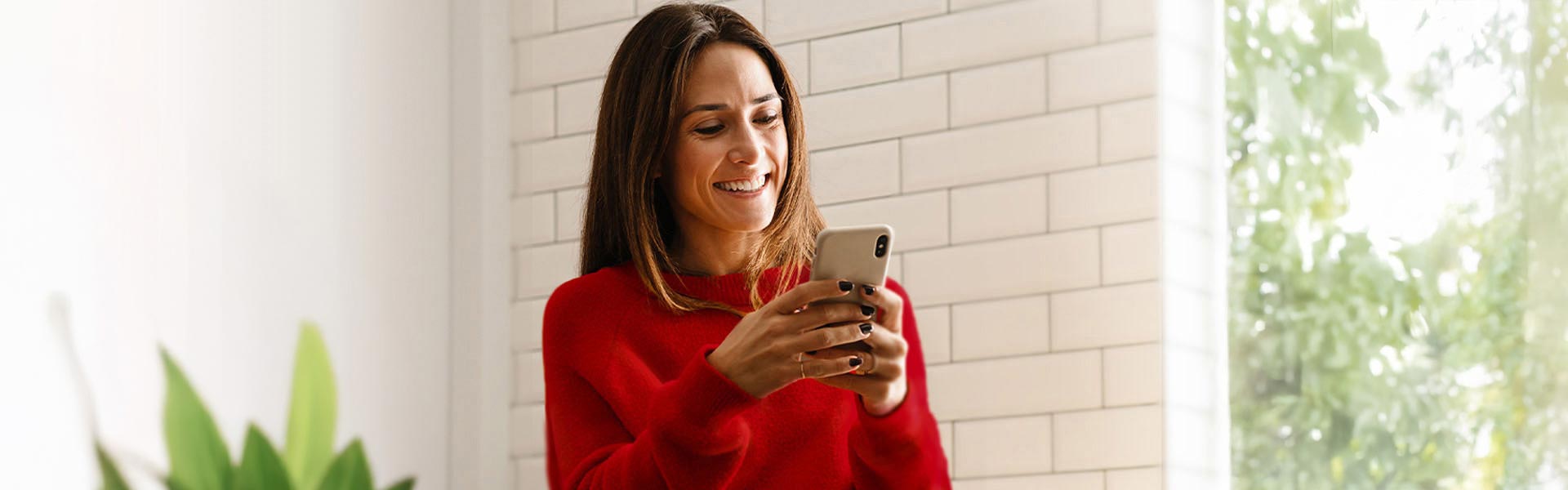 Woman in a red sweater smiling and holding her cell phone.