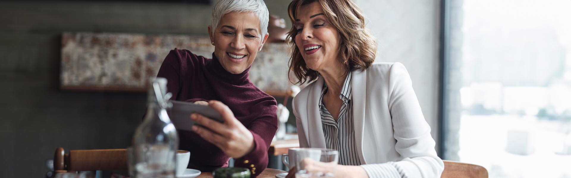 Two older women look at a cellphone together, smiling.
