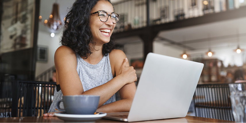 A young woman sits at her laptop smiling