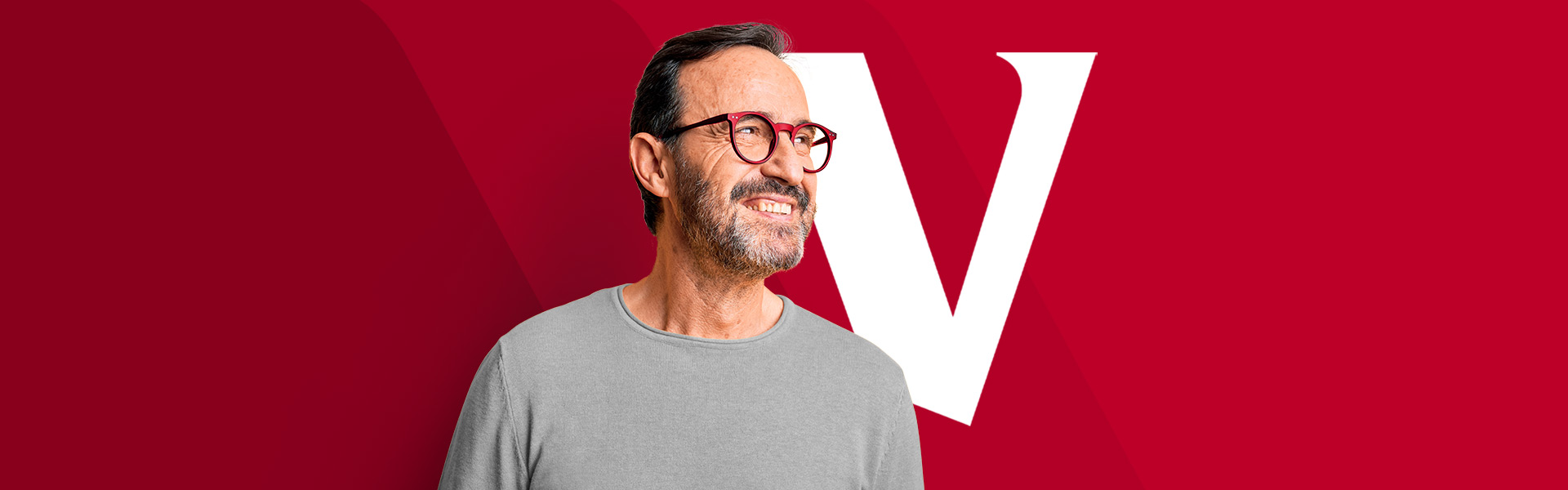 An energetic man with dark grey hair and glasses looks to his left, smiling brightly. He is standing in front of a red backdrop with a big white Vanguard 