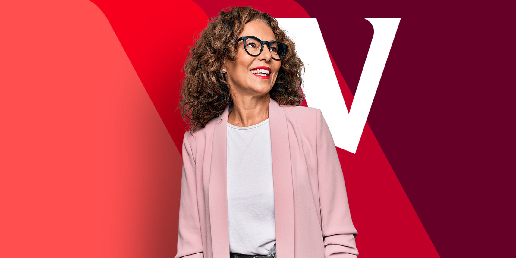 A woman smiles as she stands in front of a red banner  displaying the Vanguard V logo.