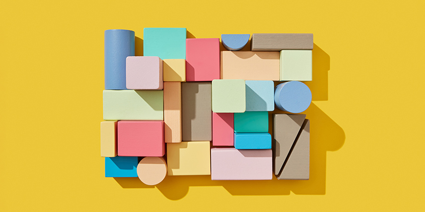 A rectangular wooden block puzzle on a flat yellow background made of colorful pieces of varying shapes and sizes.
