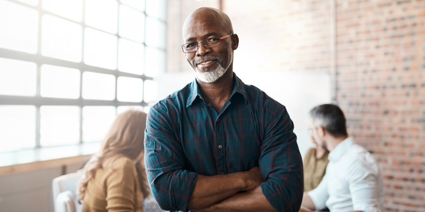 A man in a blue shirt stands with arms crossed, wearing a confident smile.