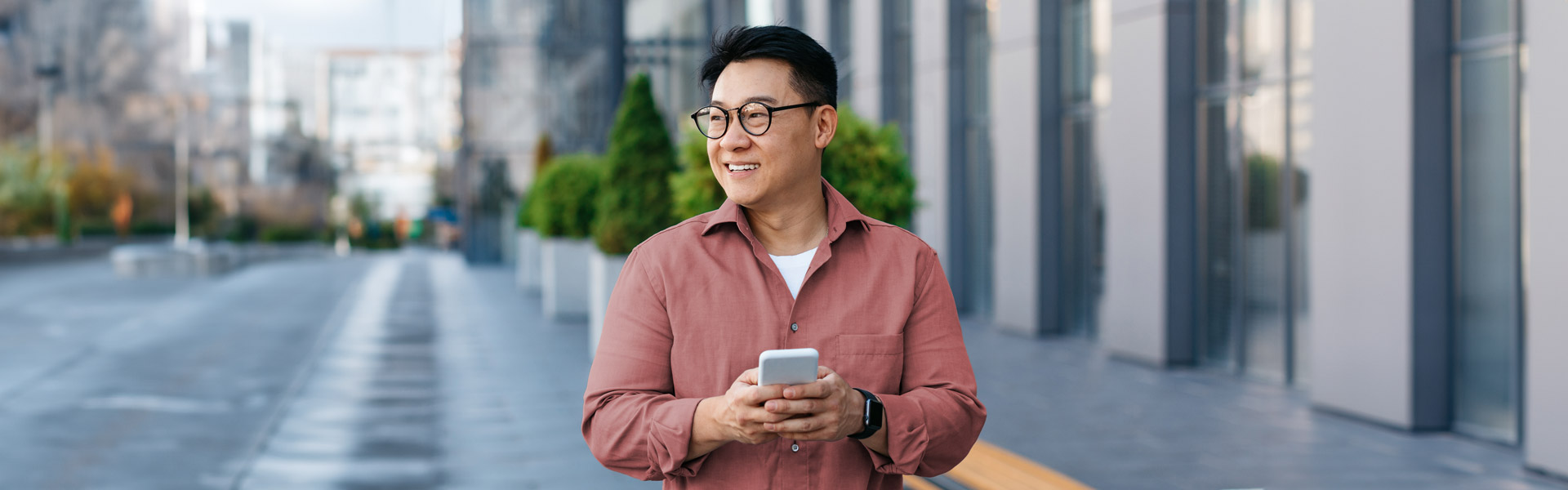 A smiling man in a red shirt reacts to good news on his mobile device.