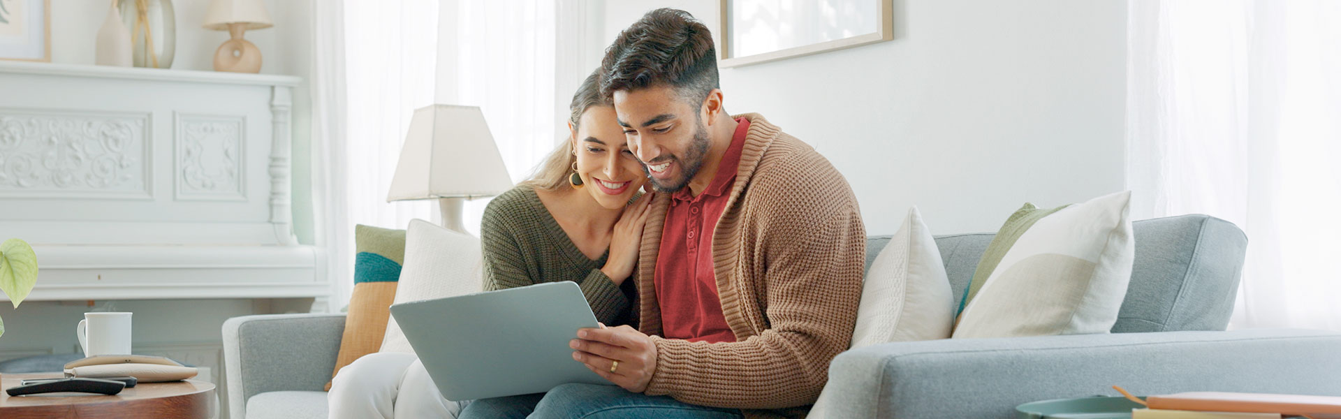 A young couple sitting on the couch together and looking at a laptop.