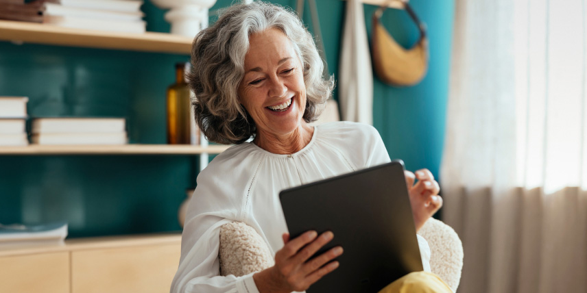 A woman smiling and sitting in a chair using her tablet.