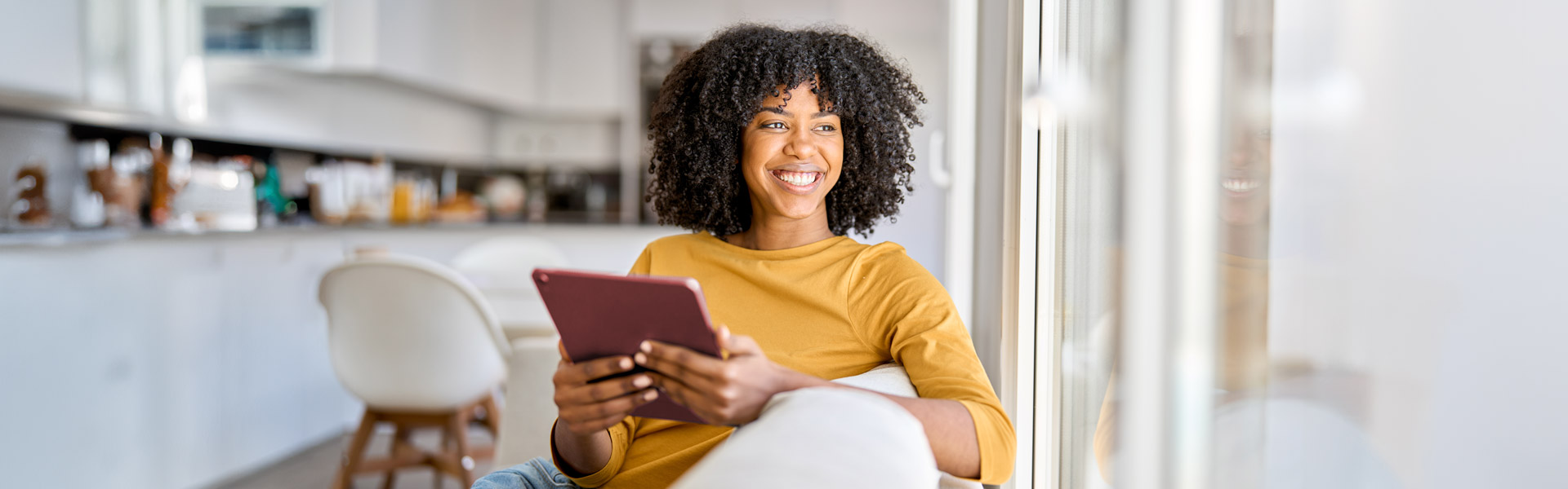 Woman on tablet smiling looking out of the window. 