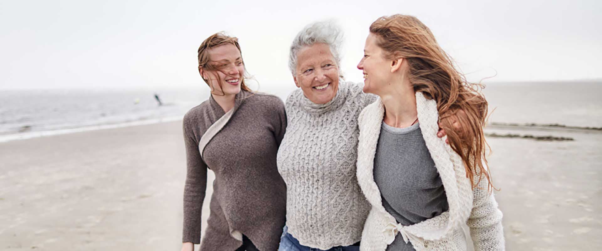 Older woman walking arm-in-arm with her two adult daughters on the beach.
