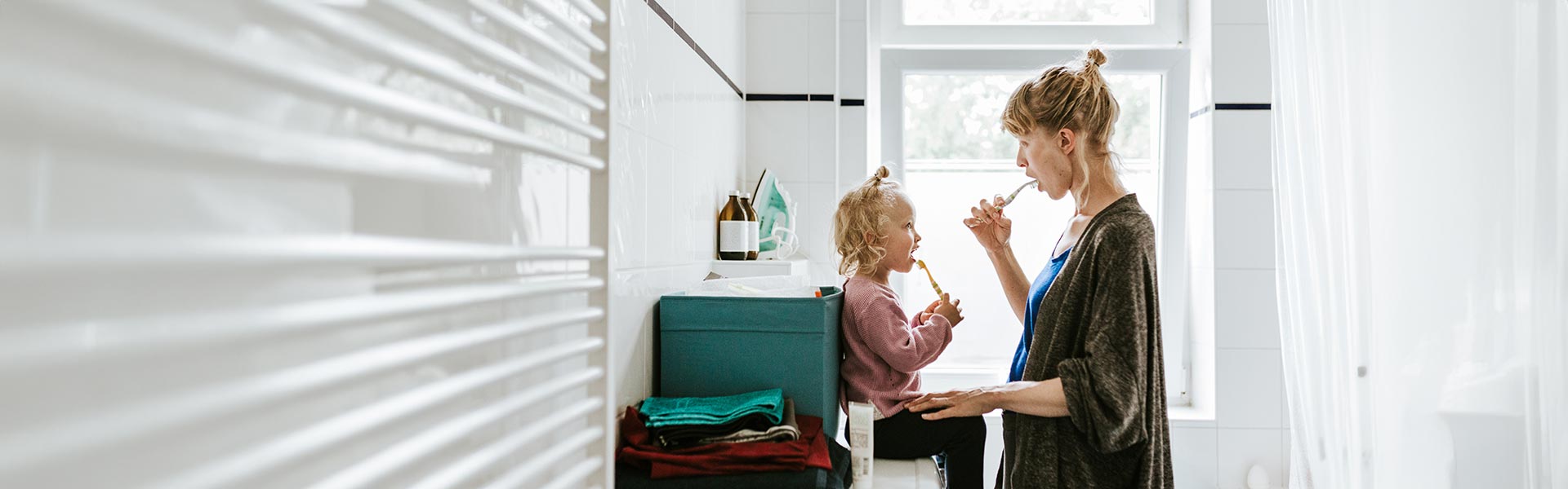 A woman teaches her daughter to brush her teeth.