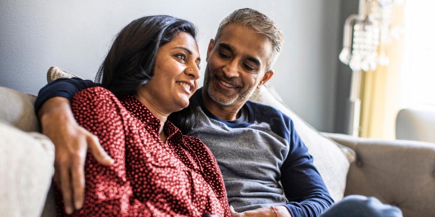 Two people sit together on a couch, with one arm around the other.