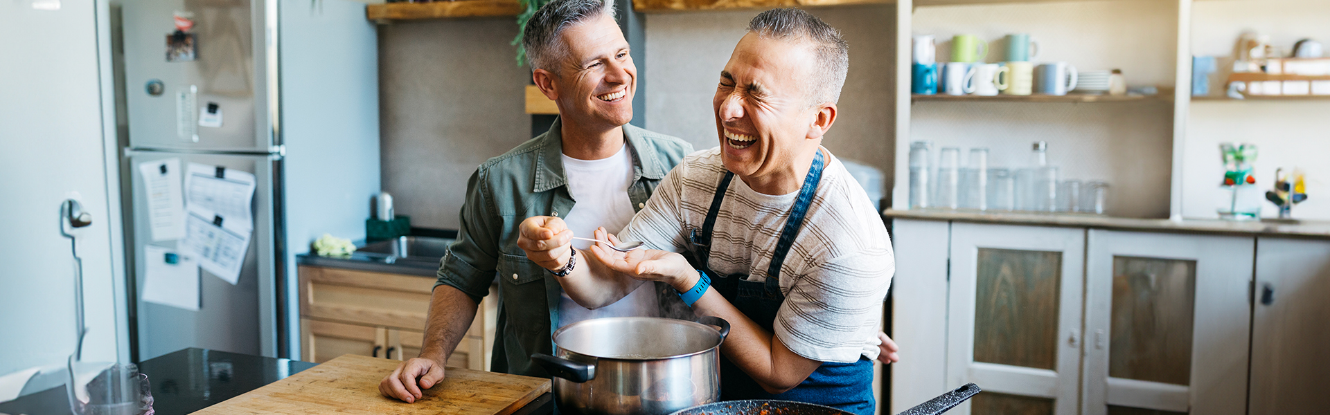 Two men laughing and cooking in the kitchen together.