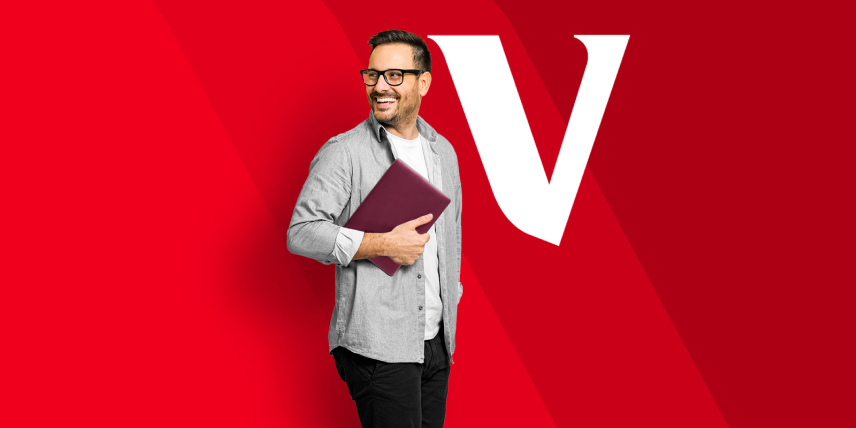 A man in glasses holding a book looking off to the side. There’s a white V in the background. 
