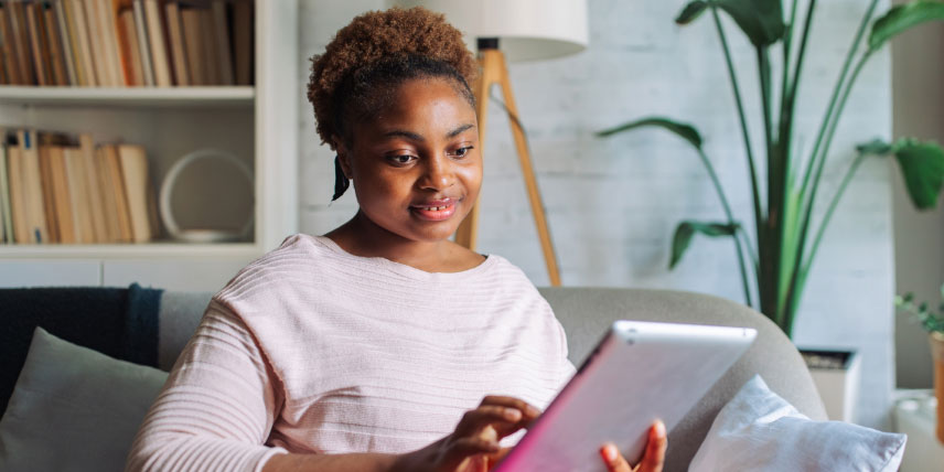 Women sitting on the couch and looking at her tablet.