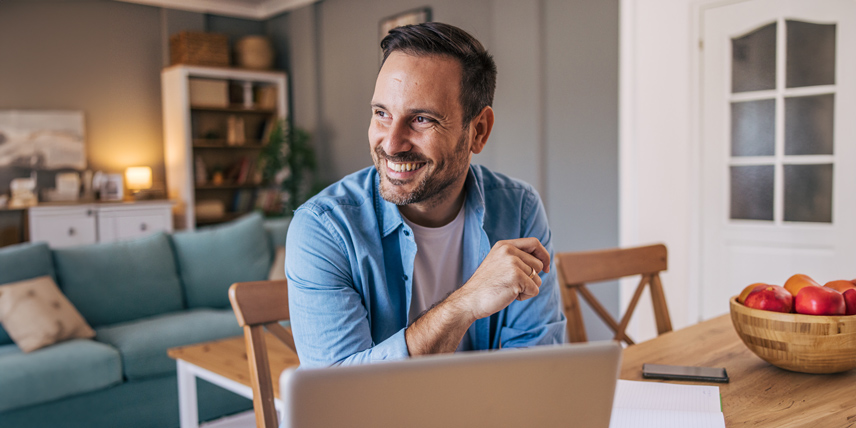 A man sitting at a table with his laptop open, smiling.