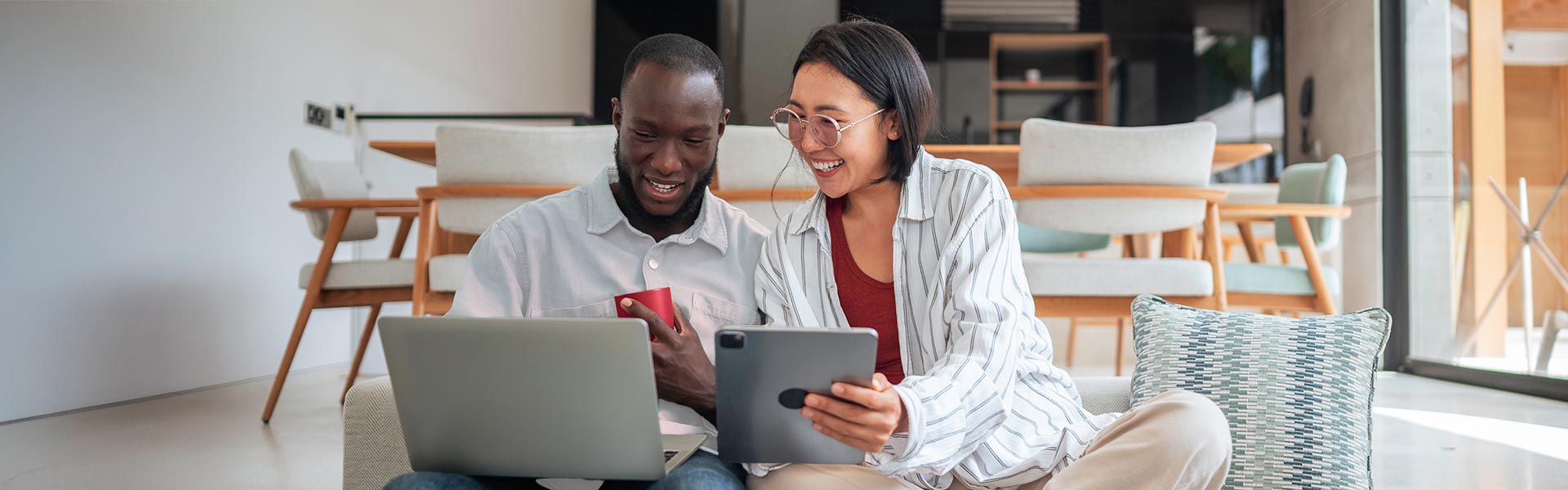 A man and woman sitting together looking at a laptop and a tablet.