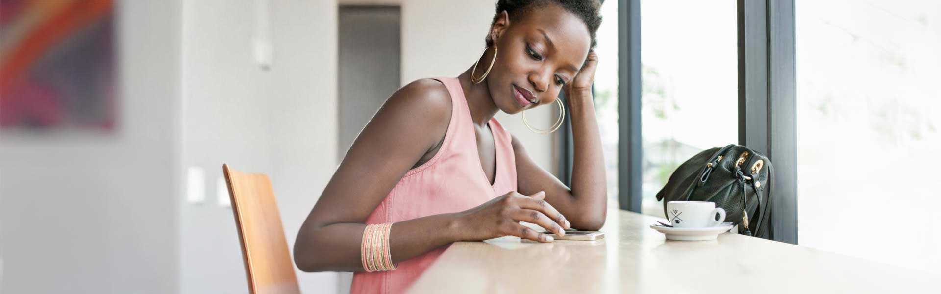 A woman seated in a coffee shop is reading on her mobile phone.