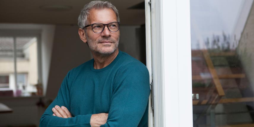 A man with glasses and crossed arms looks over his shoulder.