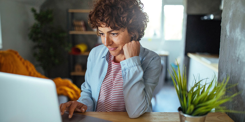 A woman views her laptop screen with an expression of confidence, resting her head against her closed fist as though fully engaged in what she's reading.