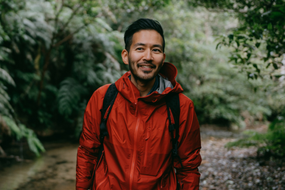 Man in red coat walking through woods.