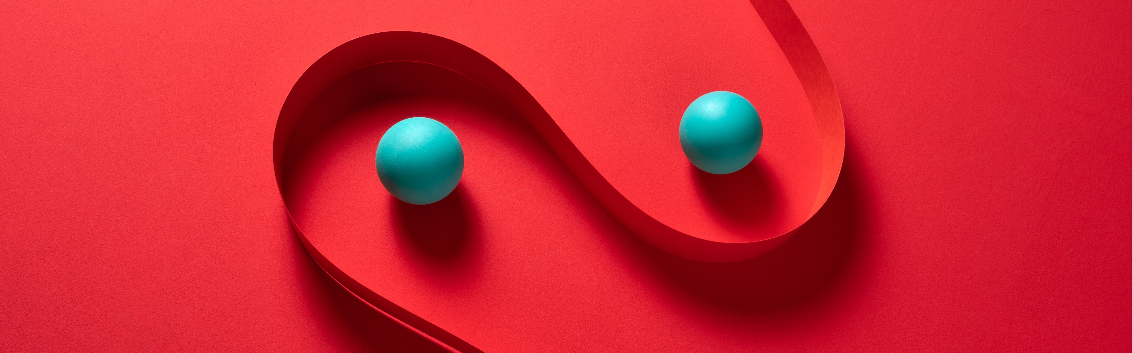 Two small teal spheres separated by a curved red ribbon on a bright red background