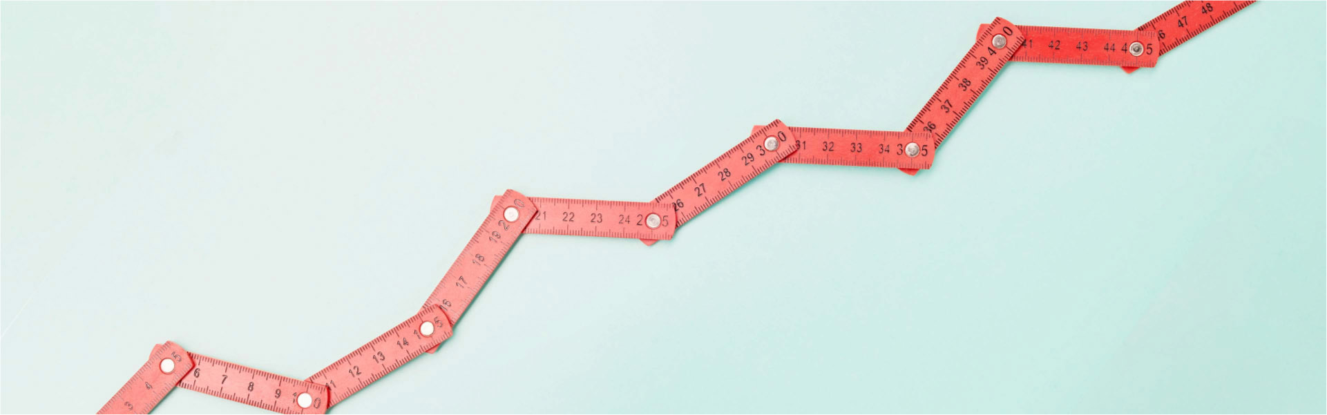 High angle view of a red folding ruler in shape of a falling stock curve on turquoise background.