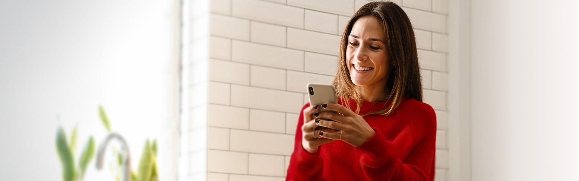 A woman wearing a red sweater smiles while looking at her phone.