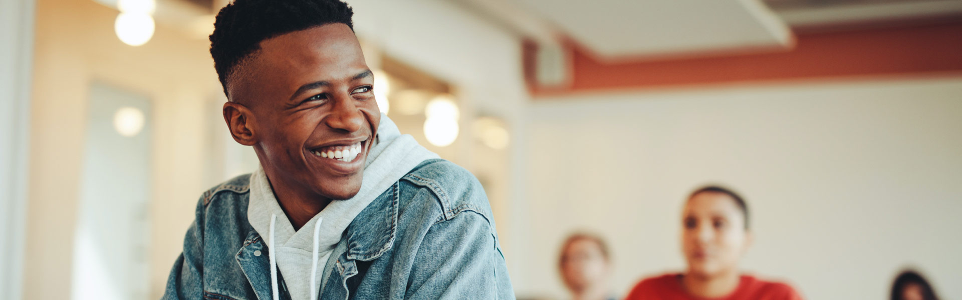 A man wearing a denim jacket smiles as he looks out of frame.