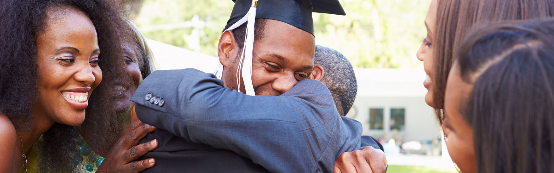 A graduate hugs his father while other family members watch and smile.