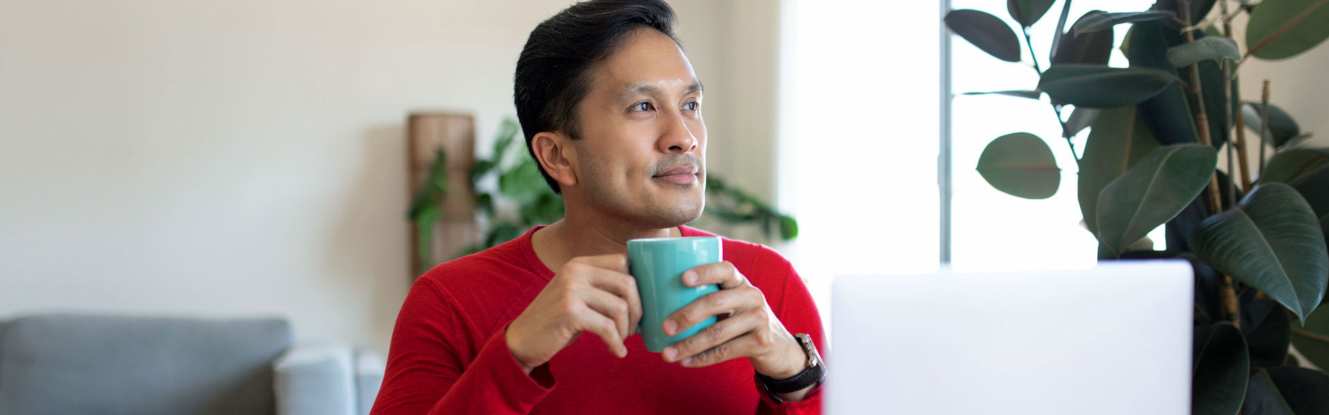 A man taking a break from his laptop to enjoy a warm beverage and reflect. 