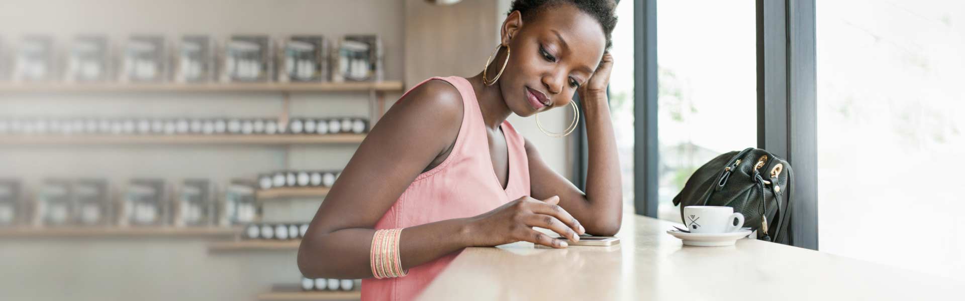 A woman seated in a coffee shop is reading on her mobile phone.