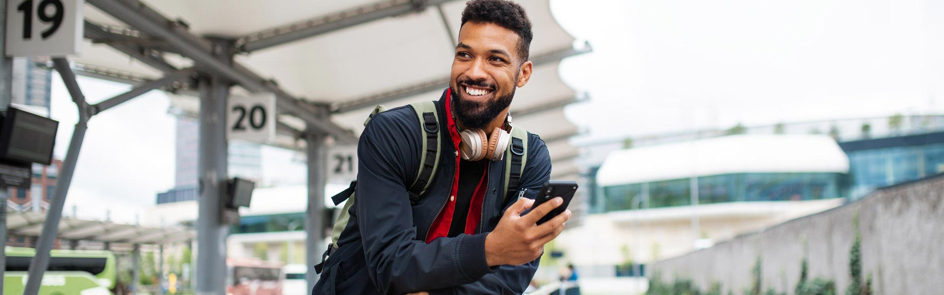 A young man outside holding his phone and smiling.