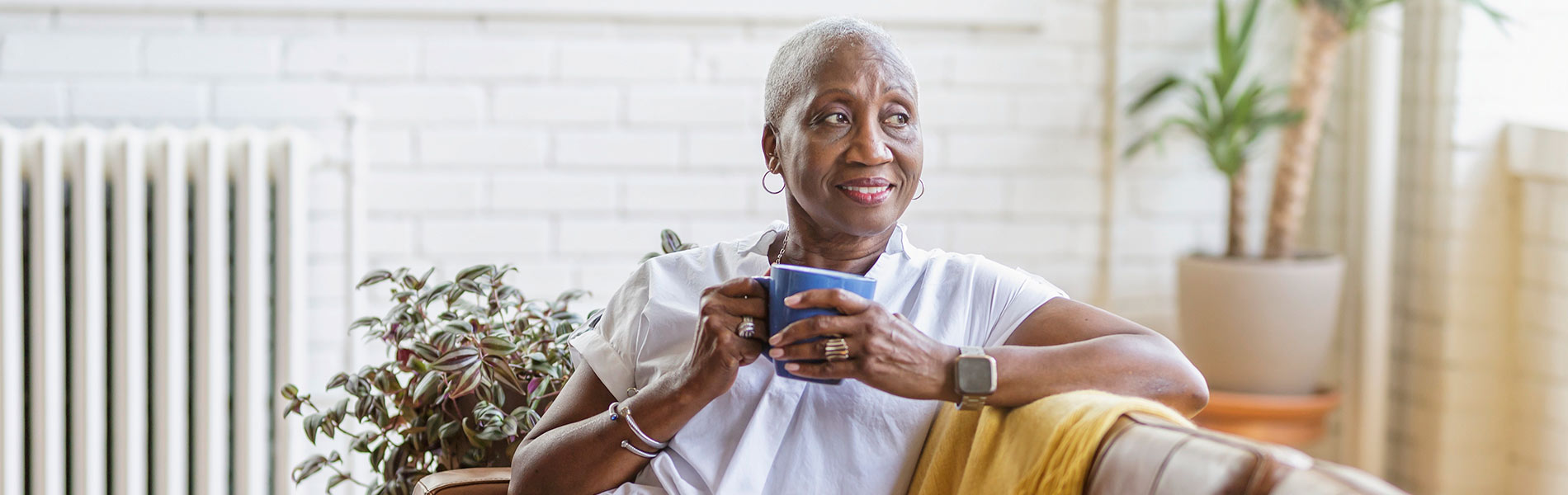 Woman sitting on a couch and holding a mug looks over her shoulder.