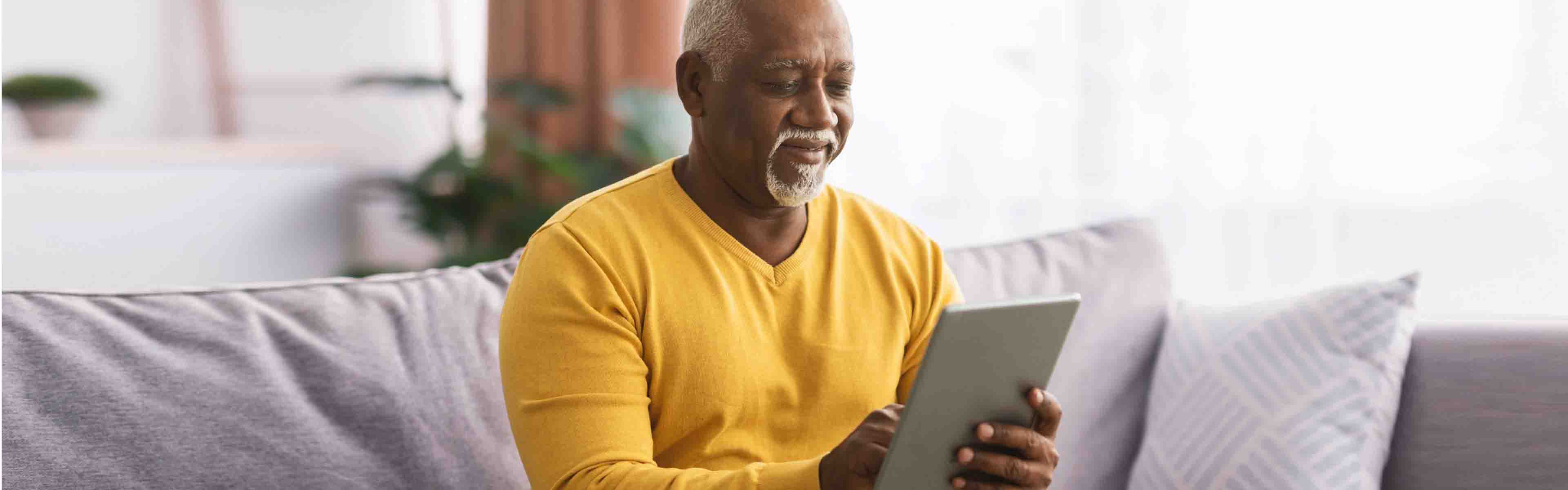 A smiling person holding an electronic device while sitting on a sofa