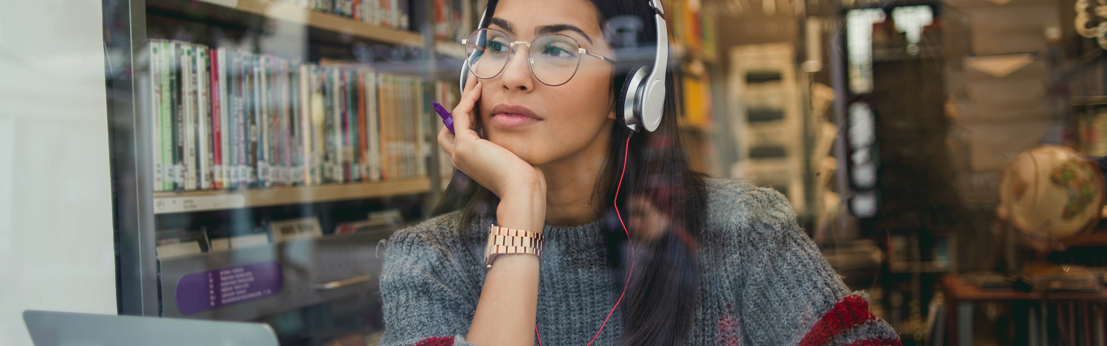 A student wearing headphones gazes over her laptop as she studies in the library.