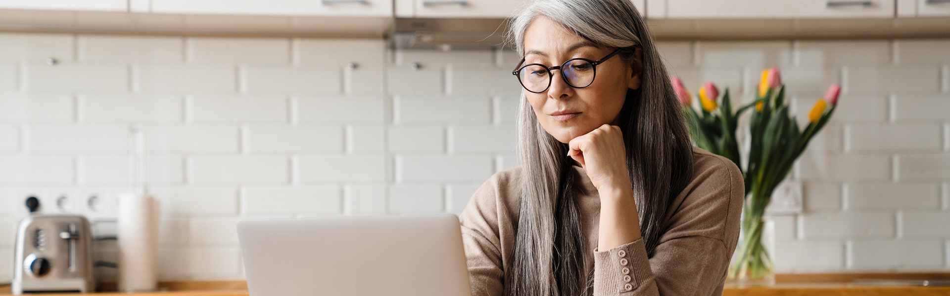 A woman sitting in her kitchen, using her laptop.