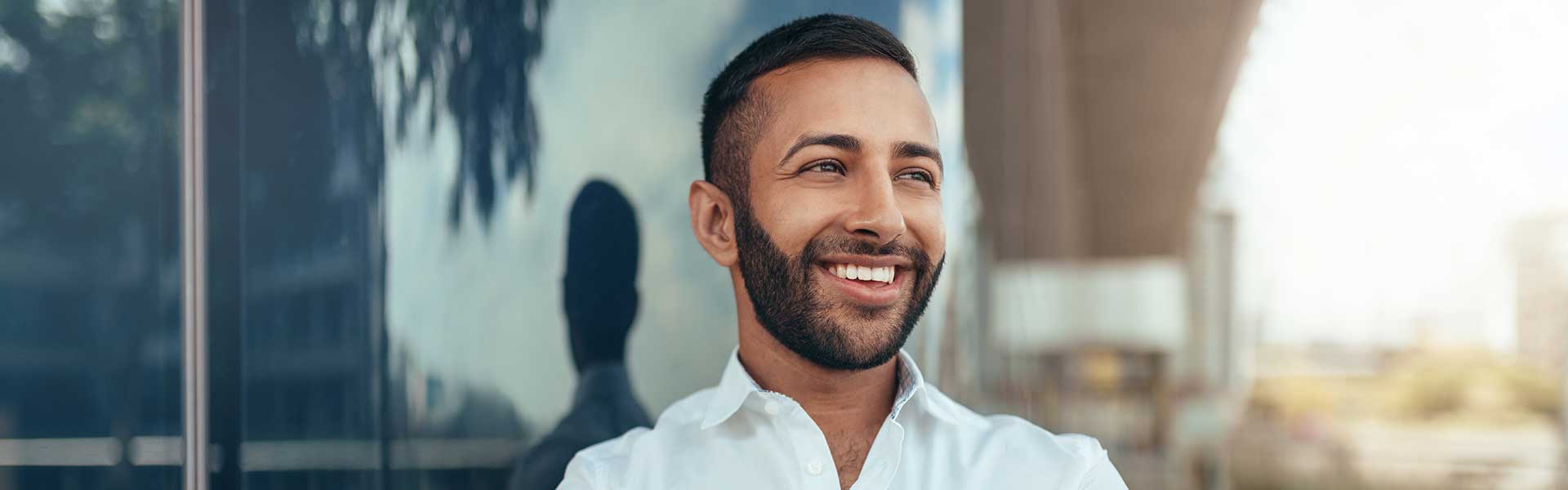 A man standing in front of a building looks out at the city scape and smiles.