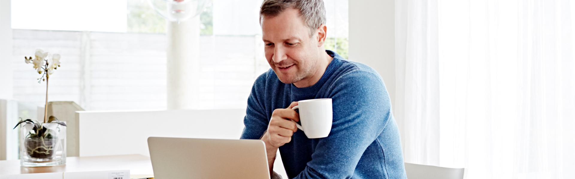 Man in blue sweater drinks coffee in home office.	