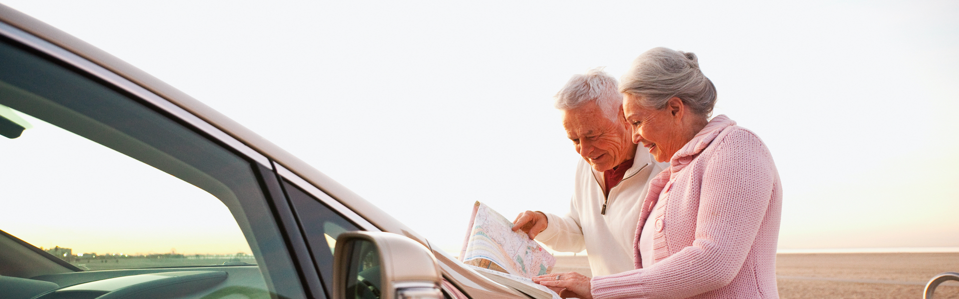 An older couple is looking at a paper map on the hood of a car.