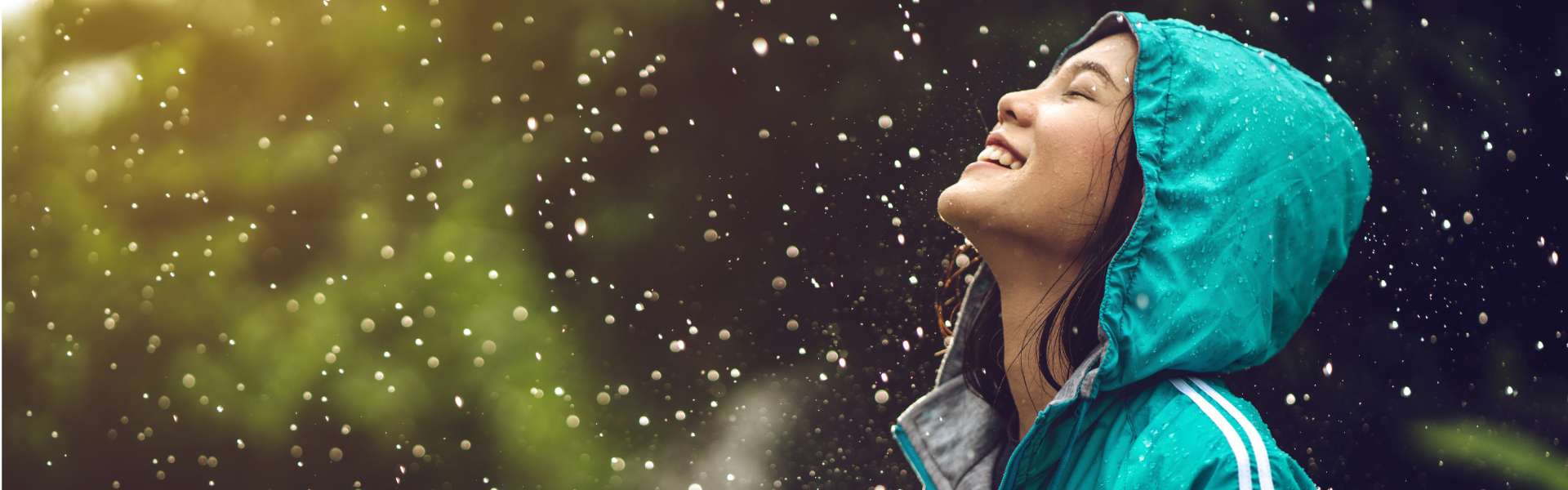 A young woman is smiling in the rain with her eyes closed.