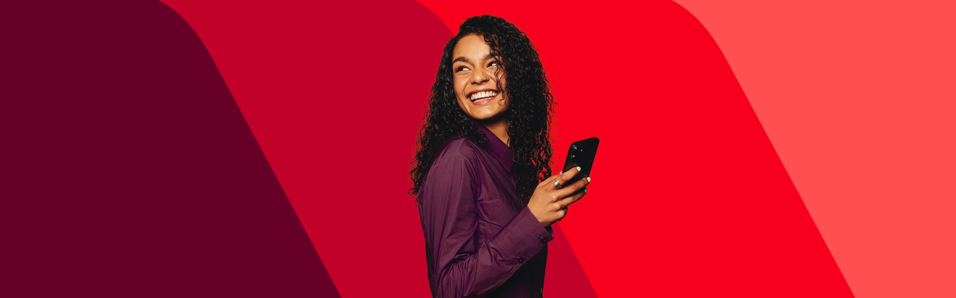 A woman is smiling and looking over her shoulder as she holds her cellphone in her hand. 