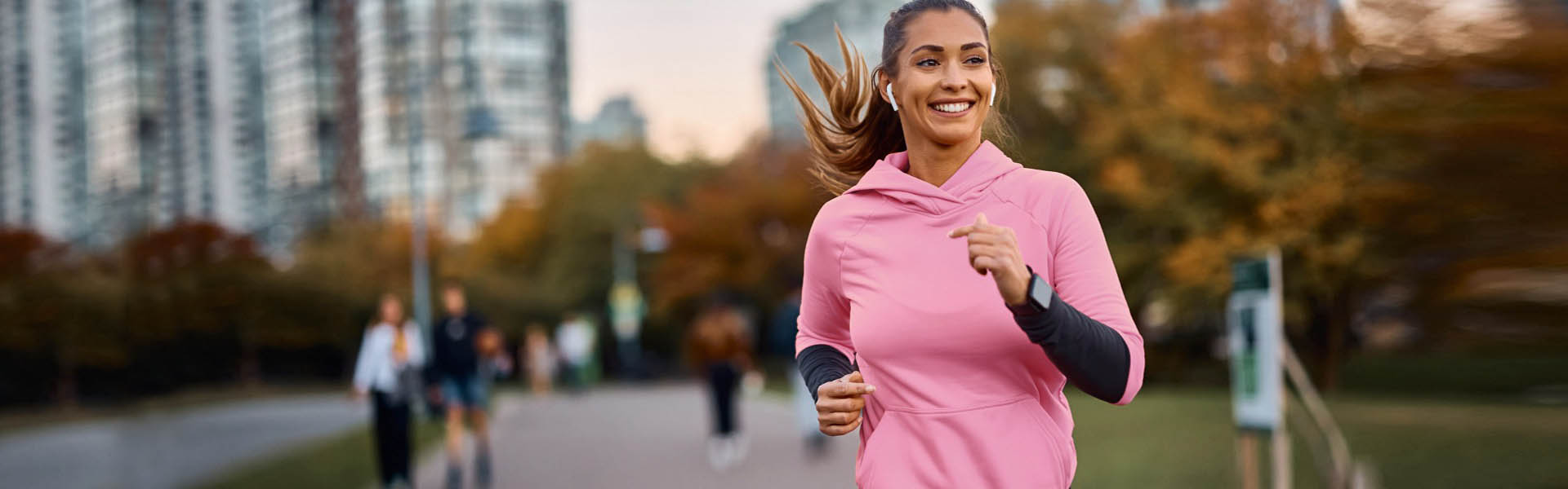 Woman smiling while jogging on outdoor path at dusk.