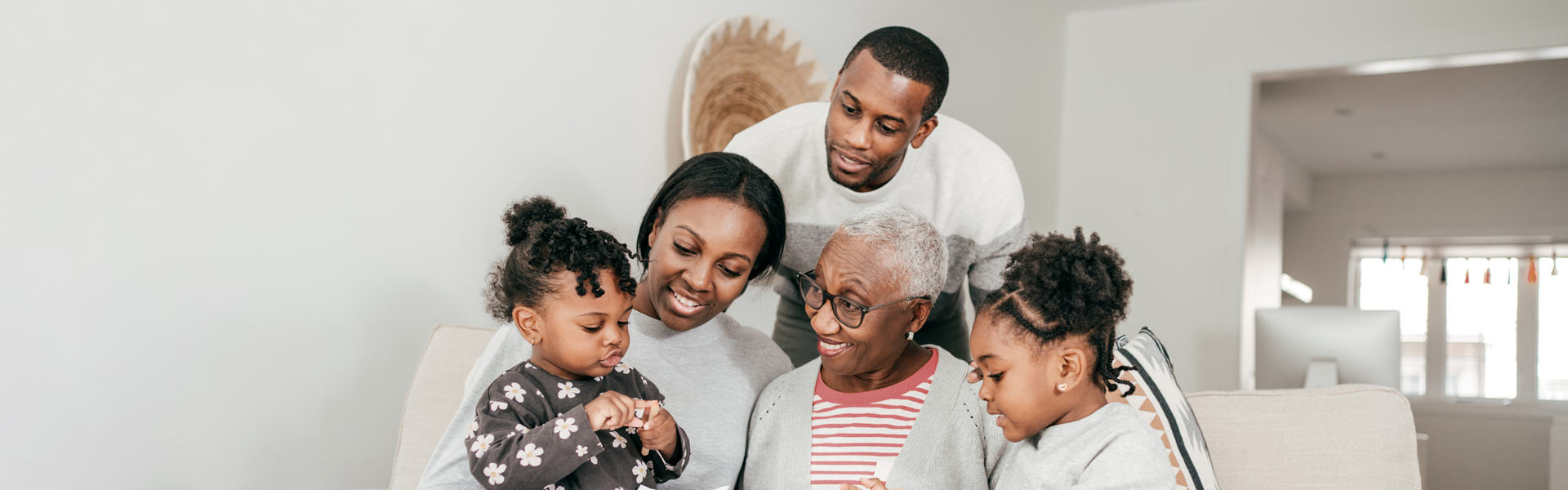 A mother, father, grandmother, and two small children sitting on a couch and spending time together.