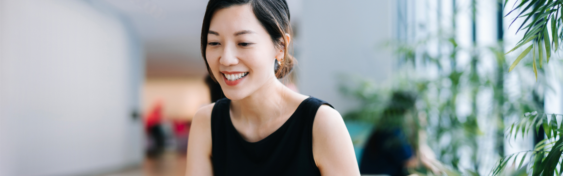 Smiling lady, in hallway filled with green plants. 	