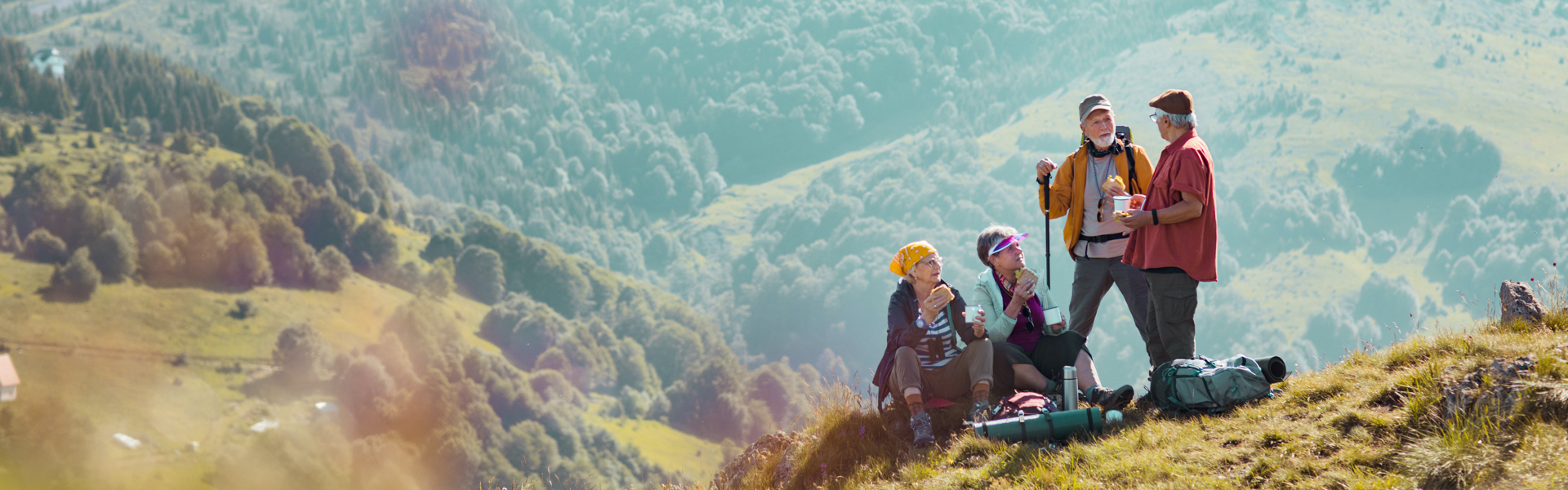 A group of older hikers are eating sandwiches on a mountainside.