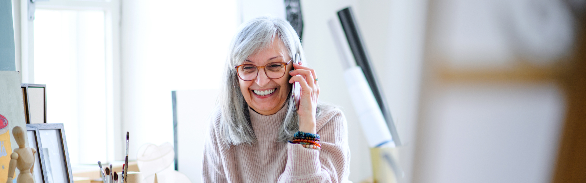 An older woman is smiling while holding a phone to her ear.